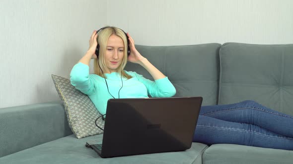 a Beautiful Young Woman Listens to Music at Home Using Headphones and a Laptop alt