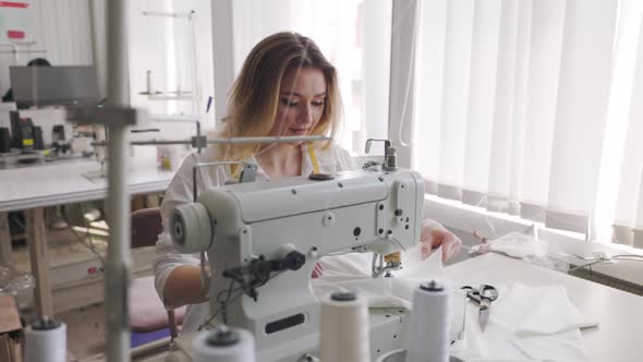 Young Beautiful Light Hair Seamstress Sews Focused in the Workplace