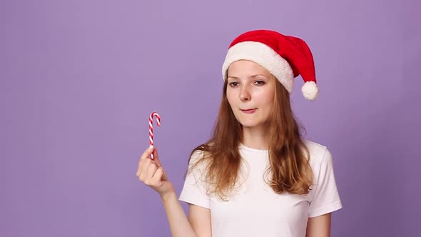 Woman White Tshirt Red Santa Claus Hat Holds Sweet Lollipop Licks Her Lips alt