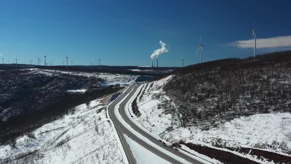 Snow Covered Mountain Highway With Smokestacks And Wind Turbines alt