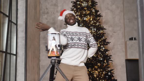 Happy African American Man in Christmas Hat Dancing Energetically in Living Room in Front of alt
