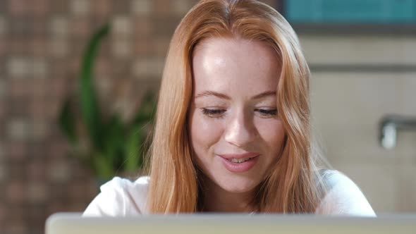 Attractive woman in kitchen working with laptop in the morning eating sandwich alt