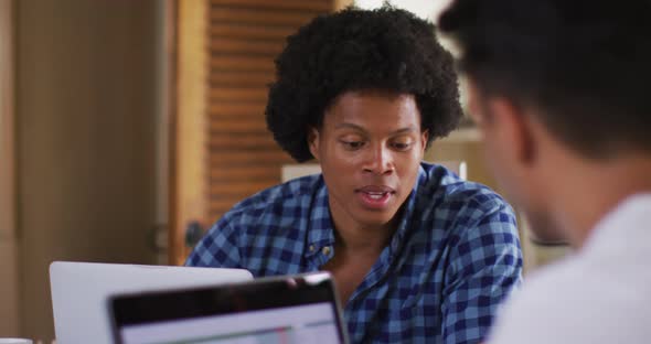 Two diverse male friends in kitchen with laptop and talking alt