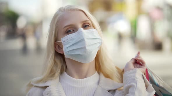 A Young Woman in a Medical Mask Throws Cardboard Colored Bags From Shops Over Her Shoulder and