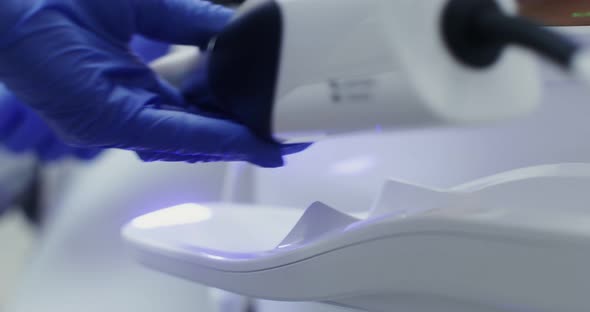 Closeup a Doctor's Hand Takes a Lamp with Ultraviolet Light to Fix a Filling alt