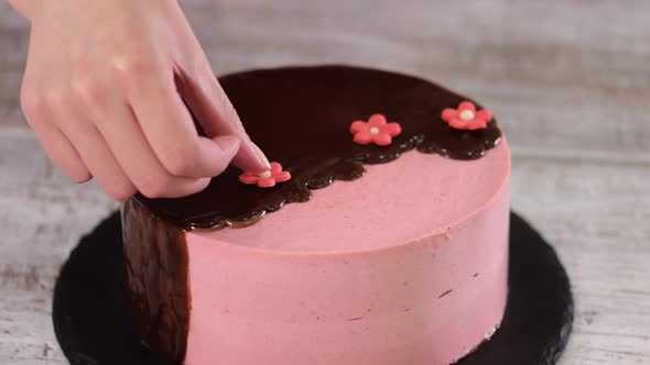 Female Hands Decorate Homemade Strawberry Mousse Cake with Sugar Flowers. alt