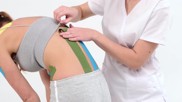 Physiotherapist sticks kinesio tapes to the small of the back of female patient, kinesiology taping alt