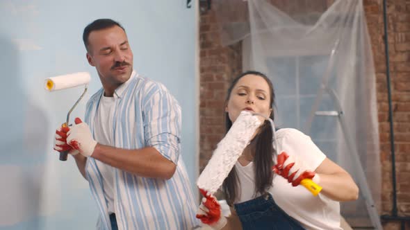Joyful Couple Redecorating Dancing and Singing with Roller Brush in New Apartment alt