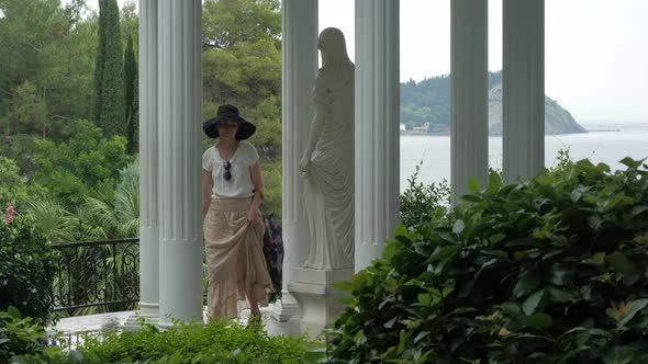 Elegant Woman Walking by Marble Statue in Aivazovsky Park, Crimea