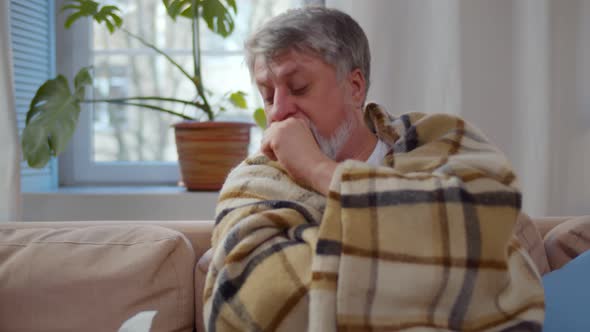 Elder Sick Man Resting on Sofa at Home Sneezing in Paper Tissue alt