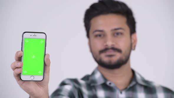 Young Happy Bearded Indian Man Smiling While Showing Phone alt