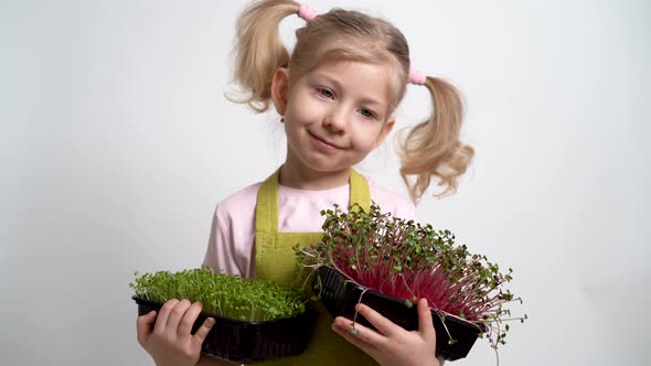 A Small Blonde Girl Smiles and Holds a Seedling of Micro Greens in Her Hands alt