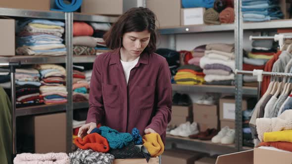 Caucasian Brunette Female Putting Box with Clothes for Recycle or Donating and Wokring with Laptop alt