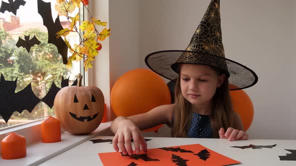 Preparation for Halloween Little Girl in Witch Costume Making Holiday Decoration Out of Black Bats alt