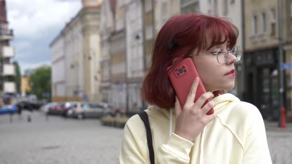 Young redhead Ukrainian teen girl talking by mobile phone on city street