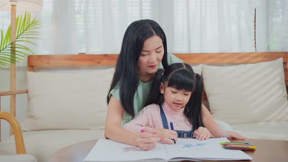 Asian little kid daughter enjoy activity having fun drawing and color picture with mother at home. alt