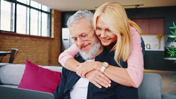 Close Uo of Affectionate Middleaged Couple Looking at a Laptop Together on a Sofa in Their Living alt