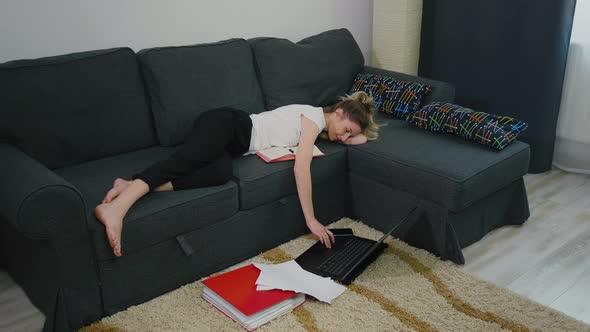 Young woman is lying on the bed at home and laptop is on the floor. alt