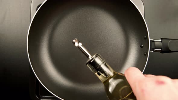 Human hands pouring olive oil on the frying pan