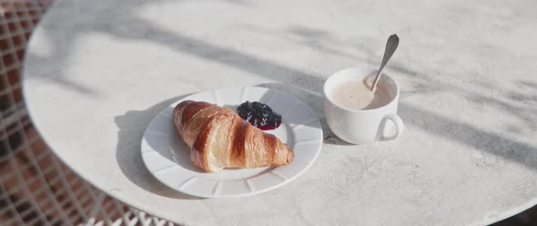 Parisian breakfast of a croissant and coffee prepared on a sunny balcony table alt