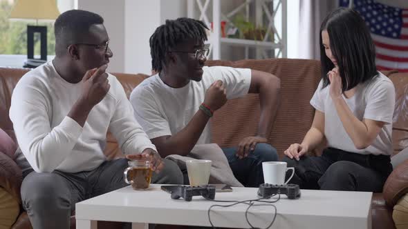Young Charming Asian Woman Bragging Necklace to African American Men Sitting on Couch in Living Room alt