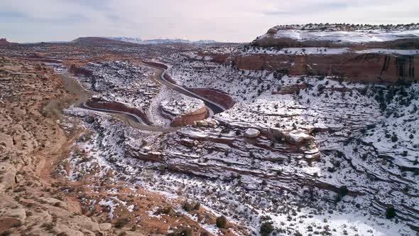 Aerial view flying through desert canyon and over winding road in the snow alt