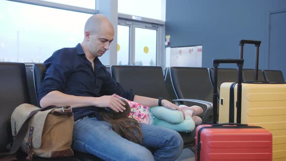 A Bored Man in the Ass Airport Waiting with a Small Tired Daughter in Her Arms Waiting for the Start