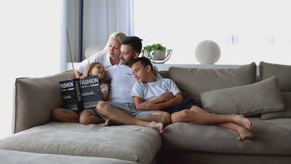 Happy Family with Two Children Reading Book Together in Living Room at Home