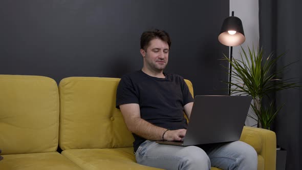 Unshaven Handsome Smiling Guy Chatting and Messaging Online on Sofa Copy Space