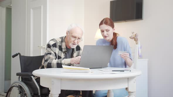 A Woman Helps a Disabled Person to Pay for Purchases Via the Internet Using a Credit Card alt