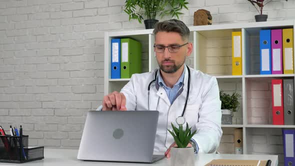 Remote doctor wears white medical coat in hospital office opens using laptop alt