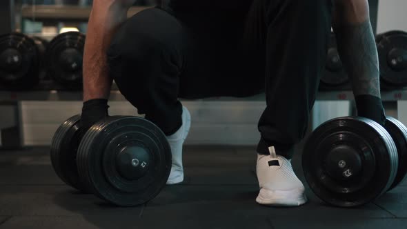 Man Picks Up Dumbbells From Floor for Exercise in Gym alt