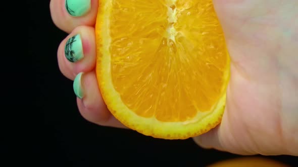 Woman's Hand Squeezes Fresh Juice From an Orange in Slow Mo on Black Background alt