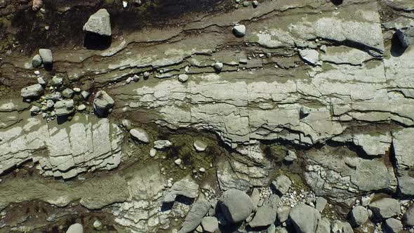 Aerial shot of young man running on a scenic rocky beach coastline. alt