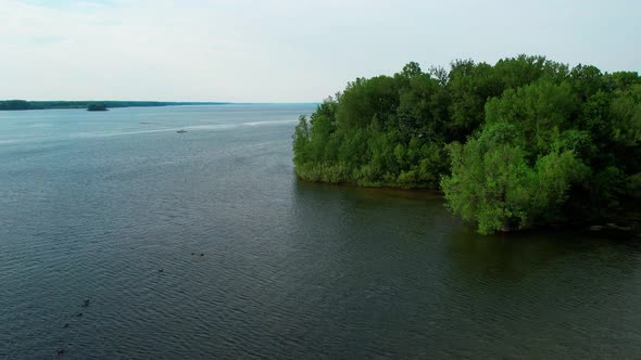 A drone shot of a beautiful calm lake in day time. Shrubs are seen which are increasing the beauty o alt