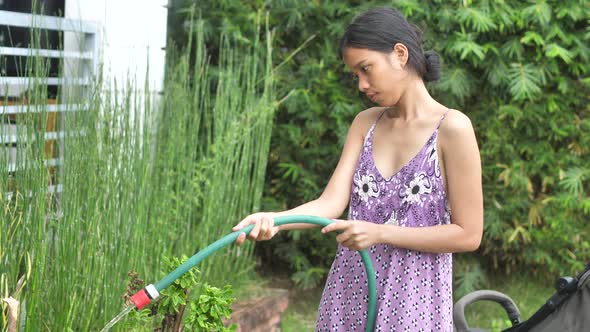 A Young Woman Carefully Pours Water on Green Plants From a Hose