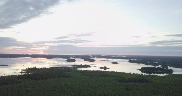 AERIAL tilt, D-LOG, Sunrise at horizon with skerries and pine forrest in the foreground, a few dead alt