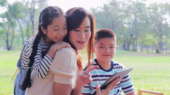 Asian family mother, son and daughter using tablet together happily and funny in the park