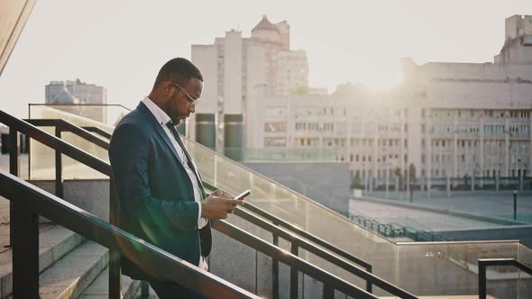 Confident African American Businessman Leaving Office Building in Evening Networking on Cellphone alt