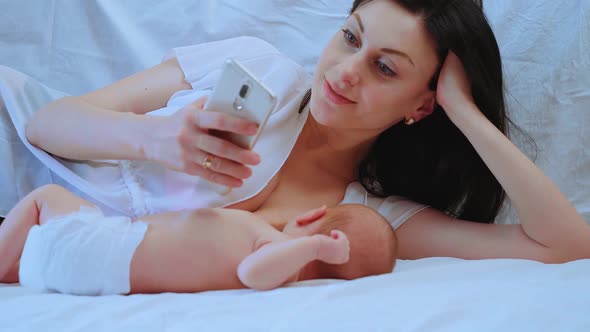 Mother with Phone Breastfeeding Newborn Baby