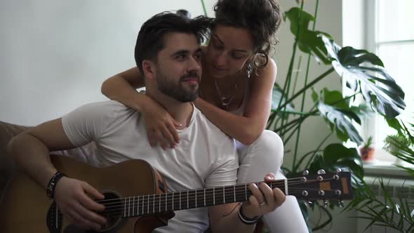 Young Woman and Man Playing Guitar While Sitting on Sofa in Modern Apartment Spbd alt