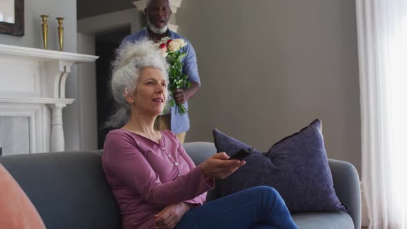 African american senior man giving flower bouquet to his wife at home alt