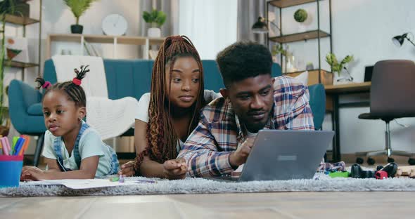 Afro American Parents Using Laptop while Daughter Drawing alt