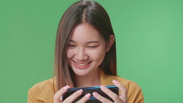 Asian Woman Looking At The Phone Screen And Holding It In Her Hands In Green Screen Studio alt