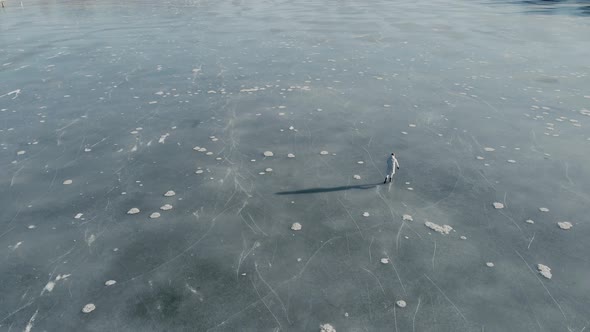 Dynamic Aerial Shot of Man Skating on a Frozen Lake on a Sunny Winter Day