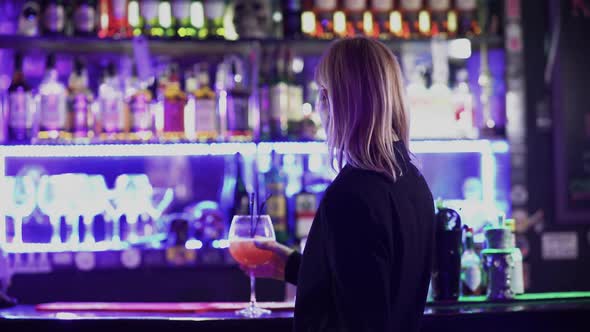 Blond Lady Drinking Cocktail Standing Near Bar Counter alt