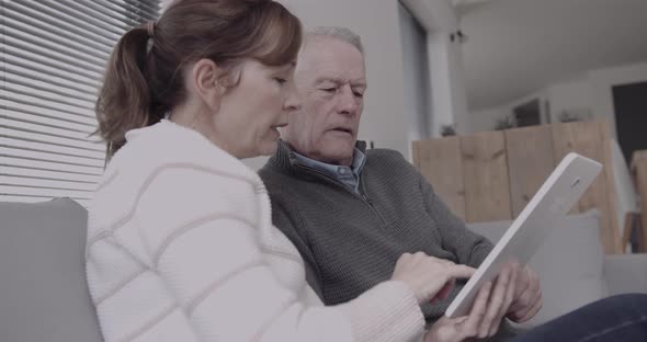 Senior adult couple at home on sofa looking at digital tablet