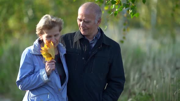 Bald Elderly Man Is Walking and Embracing His Wife, Elderly Married Couple Is Resting at Autumn Day alt