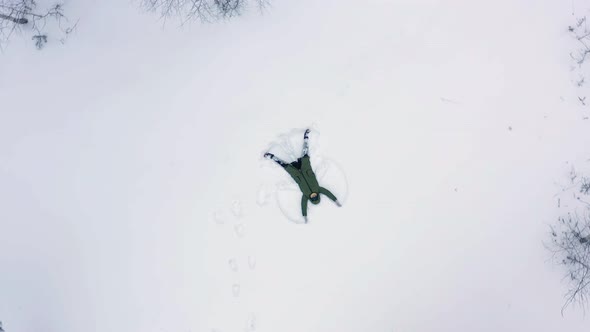 The girl lies in the snow and makes the Snow Angel with her hands. Aerial view.