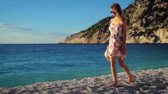 Young woman in dress walking on a beach at sunset over the sea.